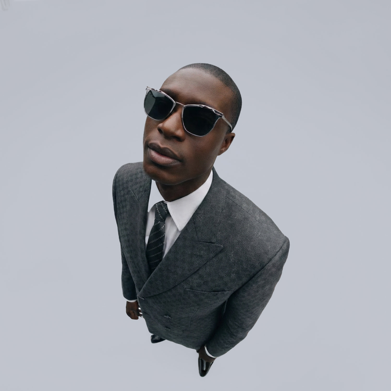Man in gray double-breasted suit wearing sunglasses viewed from high angle in studio
